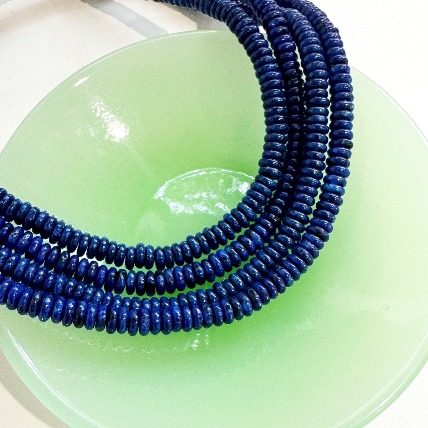 Blue beaded anklet on a green plate with a white background
