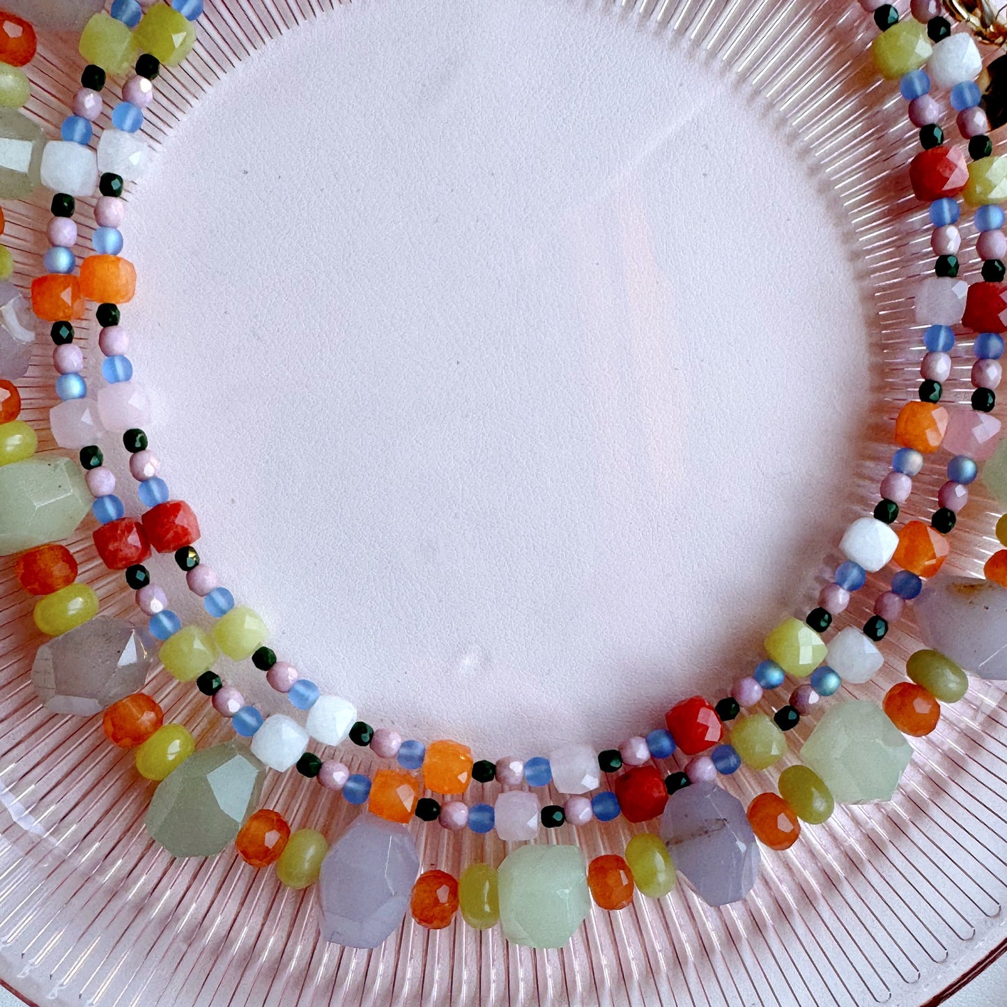 Colorful beaded necklace on a pink plate with a white background