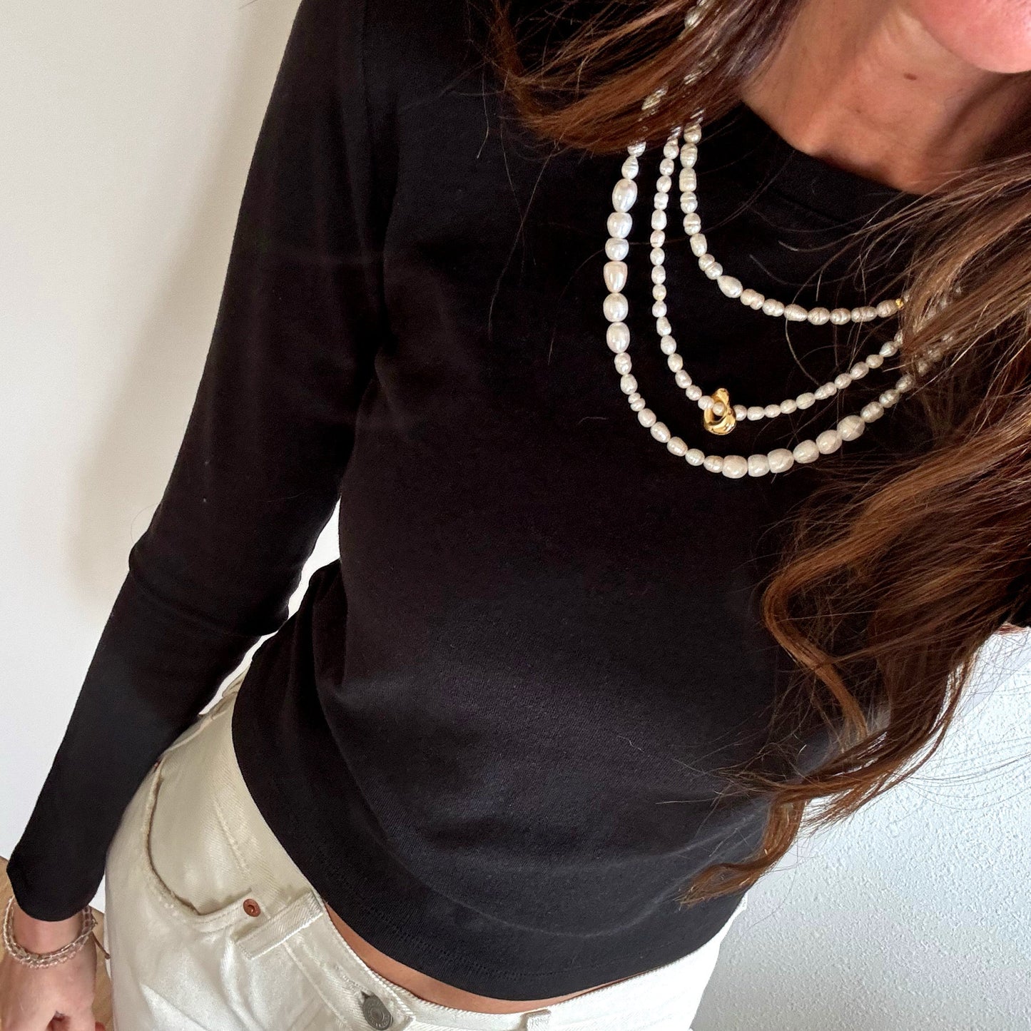 Person wearing a black long-sleeve top and light-colored pants with multiple necklaces.