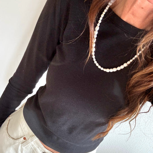Person wearing a black long-sleeve top and light-colored pants with a pearl necklace.
