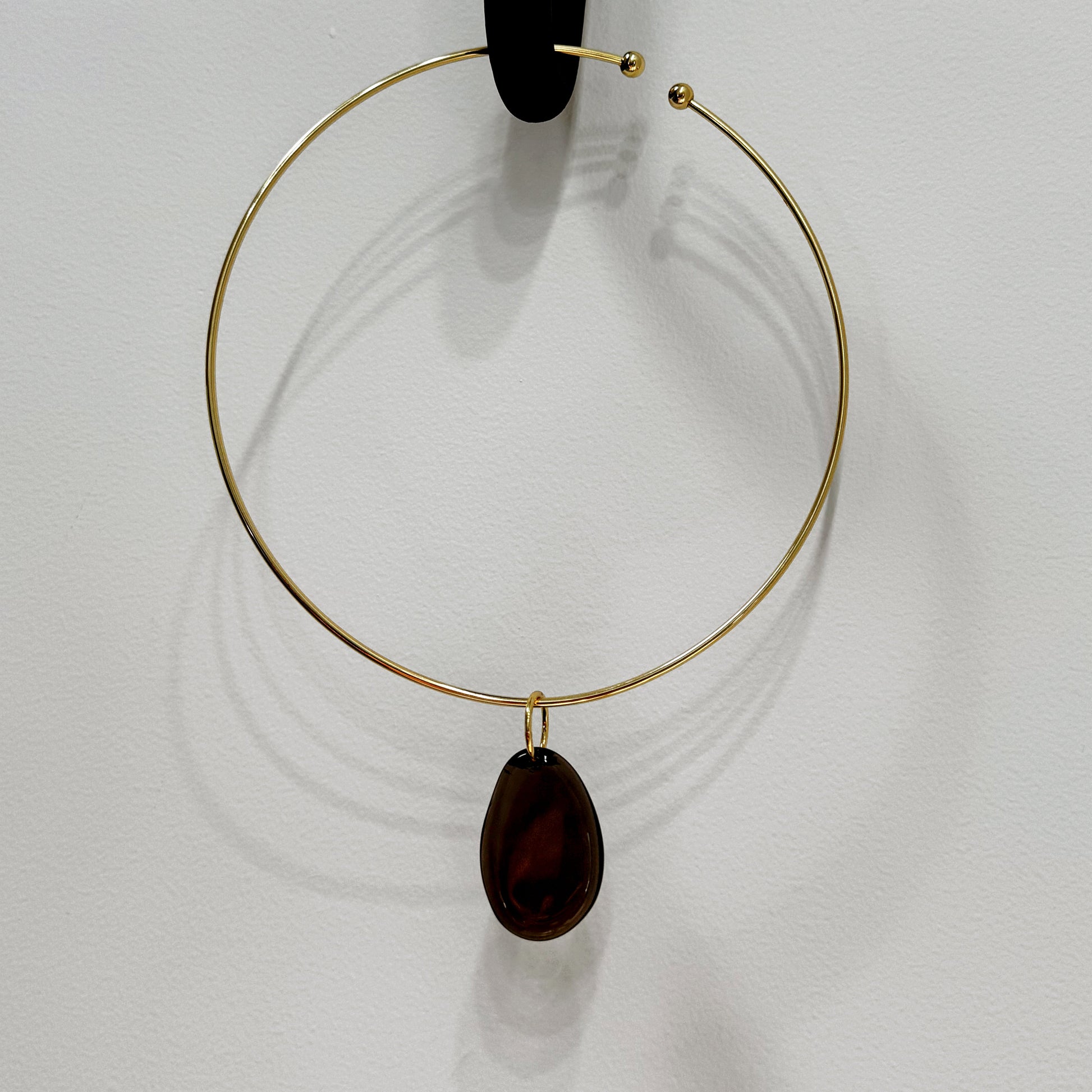 Gold hoop necklace with a dark brown teardrop pendant on a white background