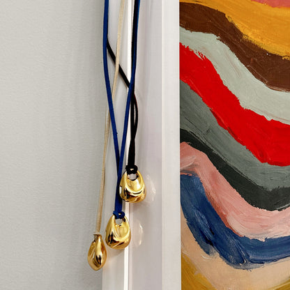 Three necklaces with gold pendants on a white surface next to a colorful abstract painting.
