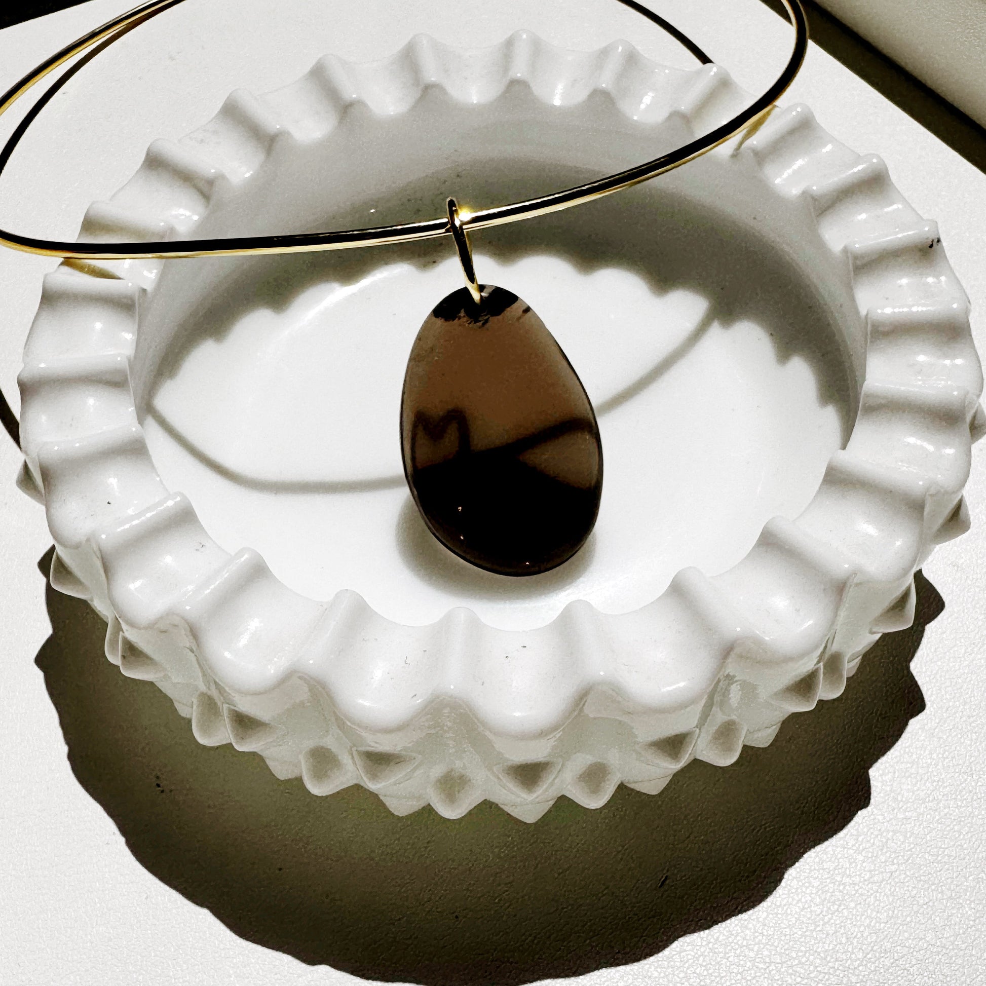 Teardrop-shaped pendant on a gold chain over a white textured surface