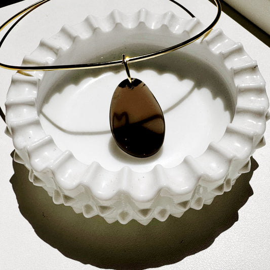 Teardrop-shaped pendant on a gold chain over a white textured surface