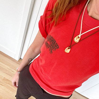 Person wearing a red t-shirt with text and dark pants on a wooden floor.
