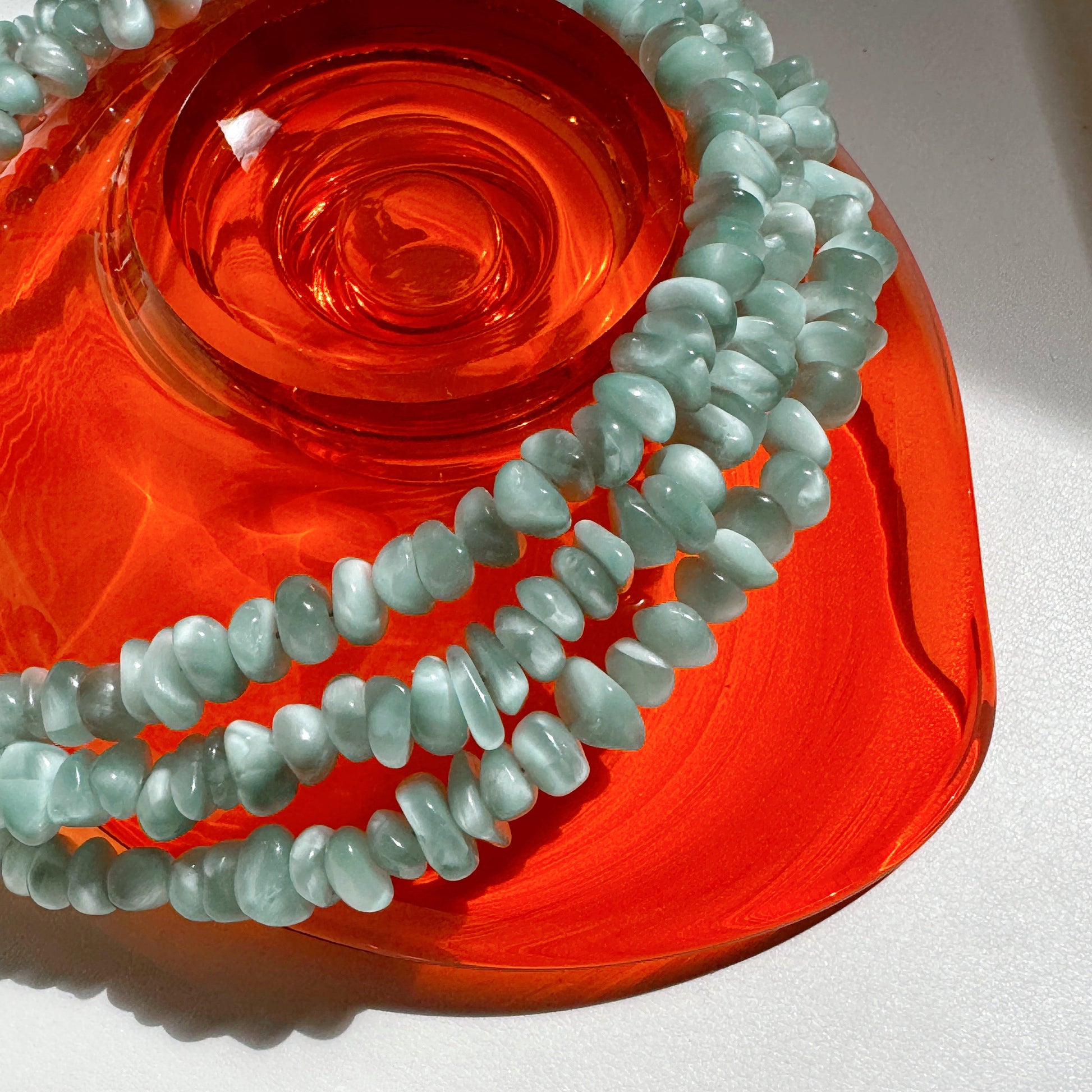Green beaded necklaces on a red glass surface