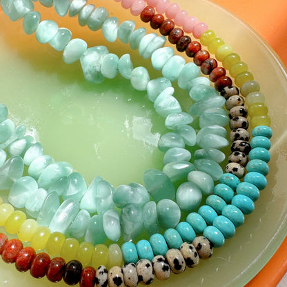 Stack of colorful beaded necklaces on a light green plate with an orange rim.