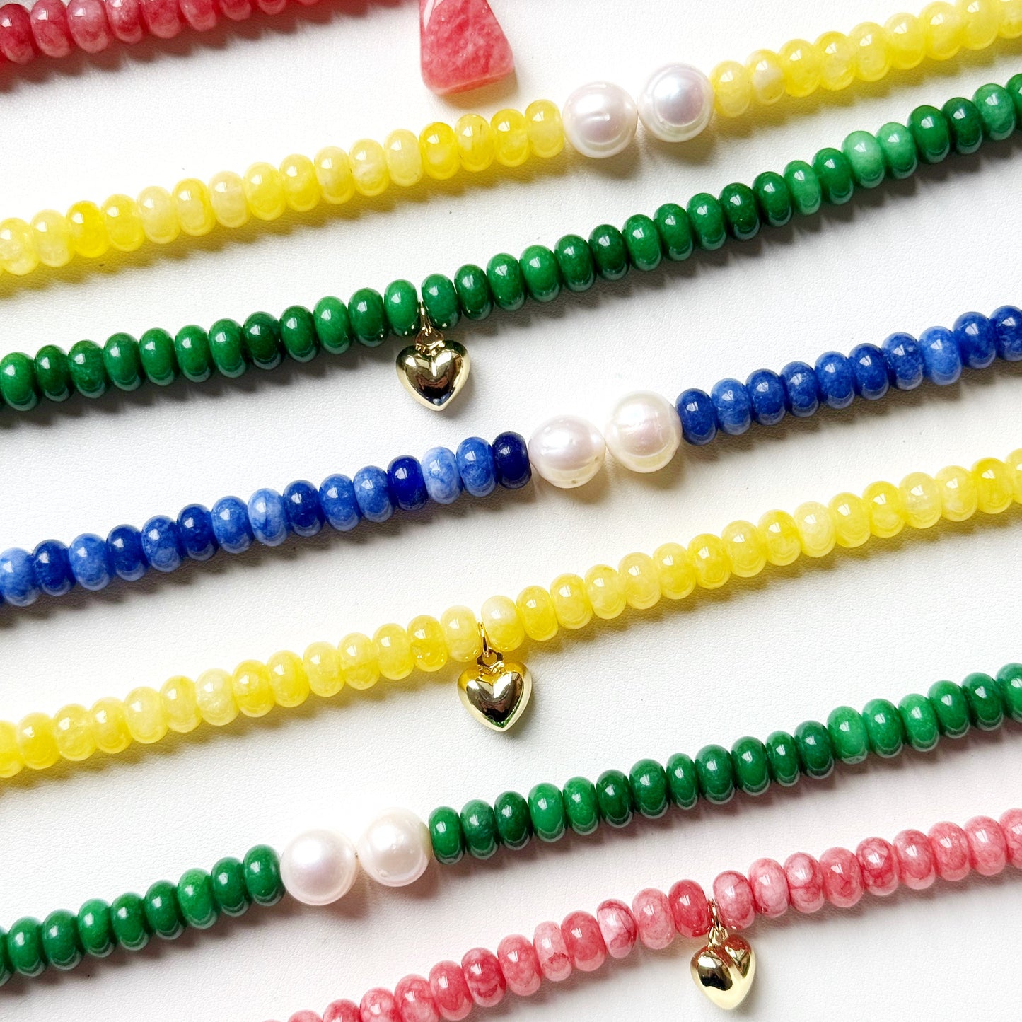 Colorful beaded bracelets with heart-shaped charms on a white surface