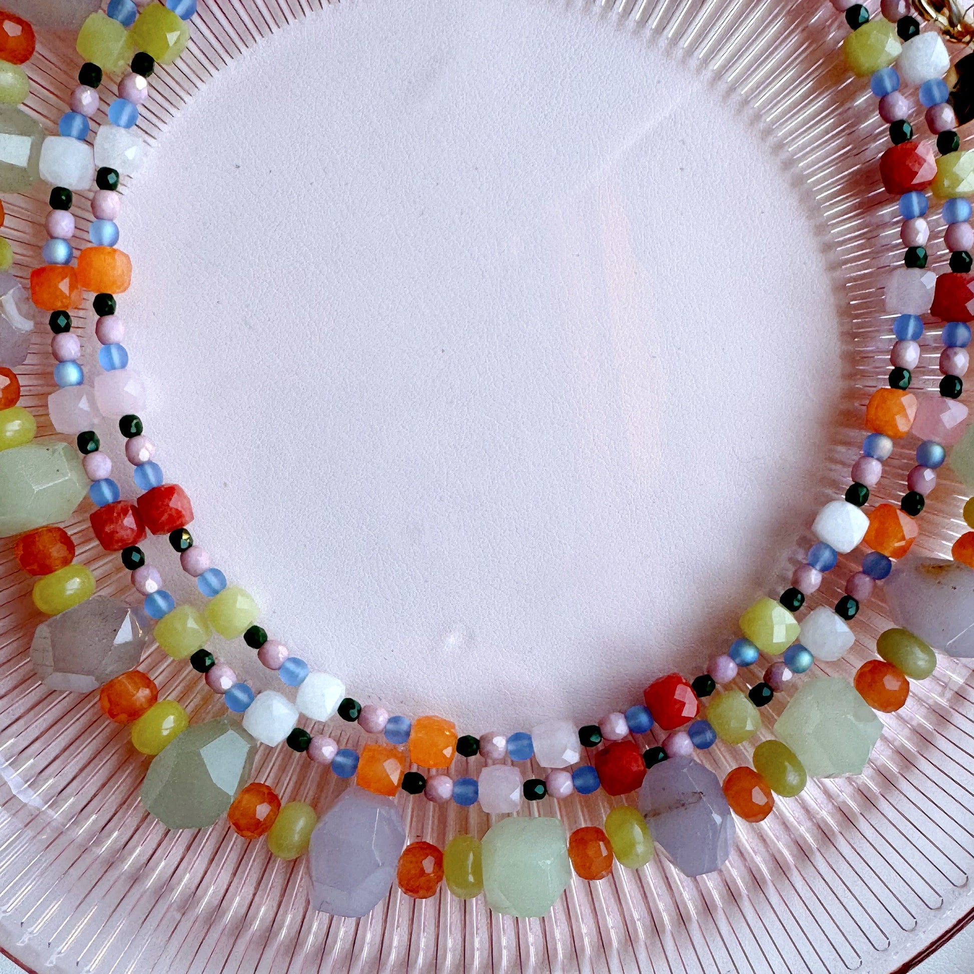 Colorful beaded necklace on a pink plate with a white background