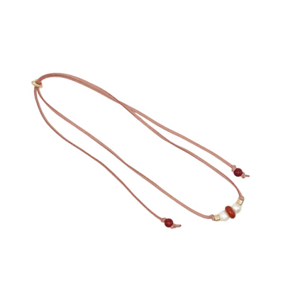 A double-strand cord necklace with small red beads and a few white pearl-like accents, laid flat on a light gray background.