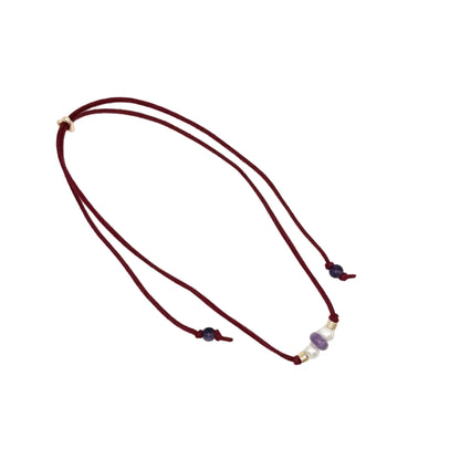 A double-strand cord necklace in deep burgundy, featuring small gold spacer beads and a central cluster of purple and white beads, displayed on a clean white background.