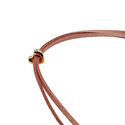 A close-up of a double-strand dusty rose suede necklace with a small gold heart-shaped clasp, set against a plain white background.