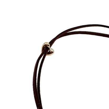 A close-up of a dark brown double-strand cord necklace with a small gold heart-shaped charm, set against a plain white background.