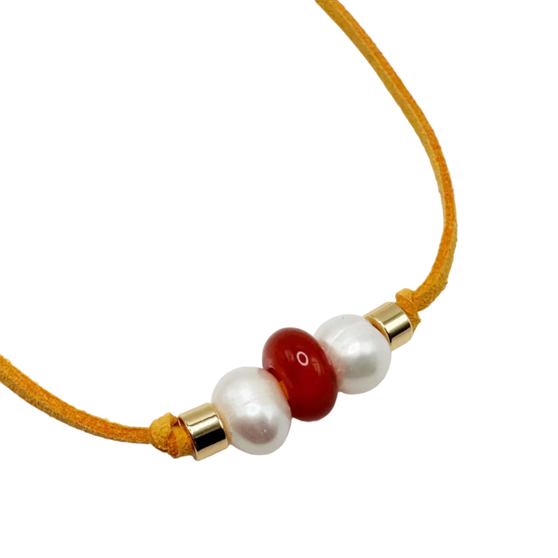 A close-up of a delicate necklace featuring a mustard yellow cord, accented with three central beads: two white faux pearls and one glossy red bead, all capped with gold-toned metal spacers.