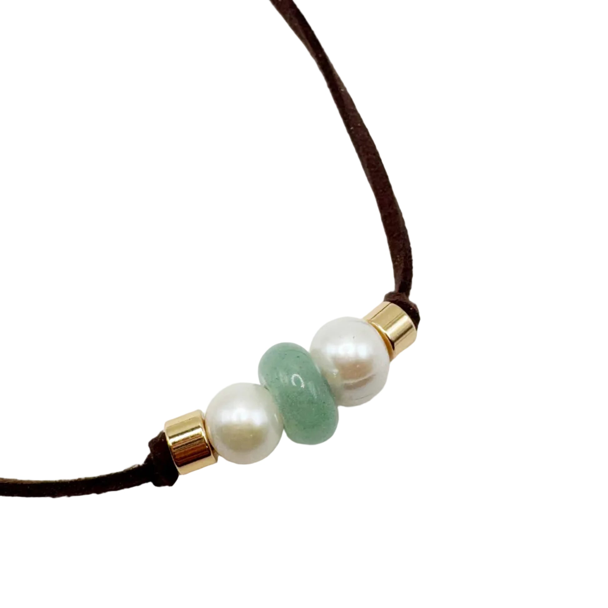 A close-up of a dark brown cord necklace featuring three central beads: two white faux pearls and one smooth light green stone, accented by small gold spacers, on a plain white background.