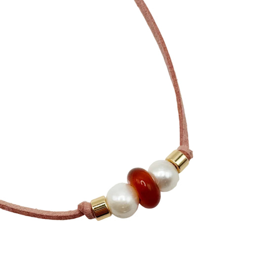 A delicate pink cord necklace featuring three central beads: a white pearl, a polished reddish-brown agate bead, and a white pearl, separated by small gold spacer rings, shown on a plain white background.
