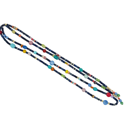 A long beaded necklace laid diagonally on a plain white background. The necklace features dark navy blue beads with small colorful accents in red, yellow, orange, green, pink, and light blue.
