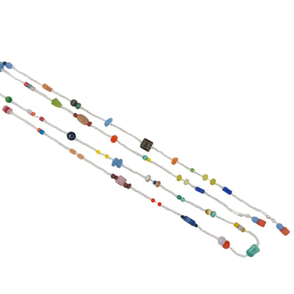 A long silver chain necklace with small multicolored beads and charms, laid diagonally on a plain white background.