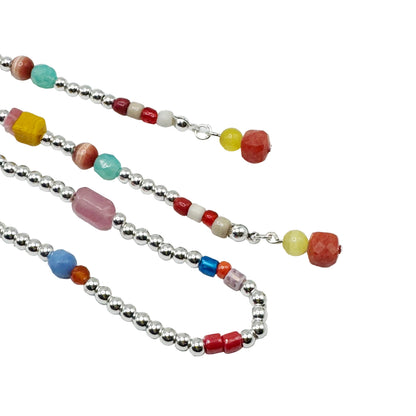 A beaded necklace with silver-toned round beads and colorful accent beads in red, yellow, turquoise, pink, blue, and white, laid out on a plain white background.