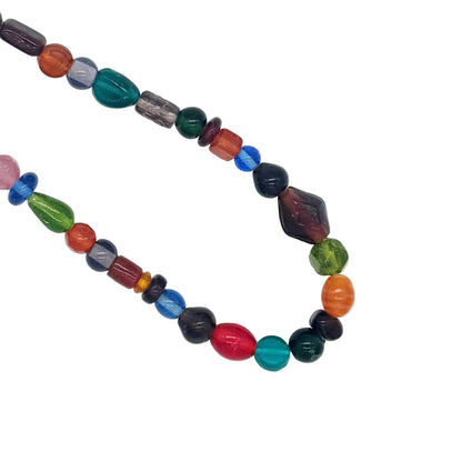 A multicolor beaded necklace made of polished gemstone beads in various shapes and colors, arranged in a loop on a plain white background.
