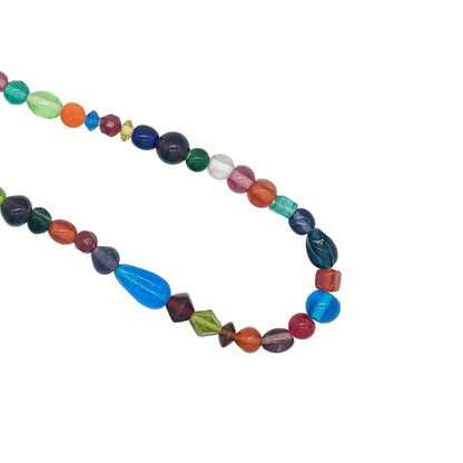 A multicolor beaded necklace made of faceted gemstone beads in various colors and shapes, arranged in a loose circle on a plain white background.