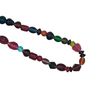 A multicolor beaded necklace made of polished gemstone beads in various shapes and colors, including dark blue, green, red, orange, pink, and turquoise, arranged on a plain white background.