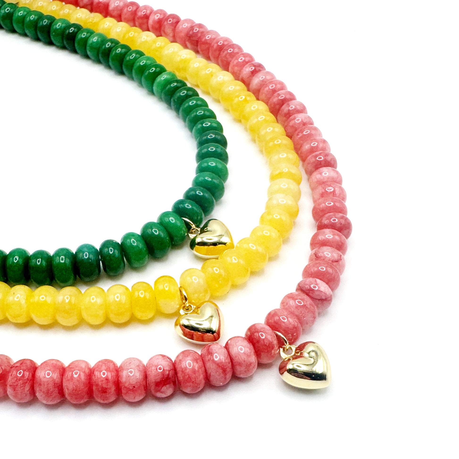 Three beaded bracelets in green, yellow, and pink with gold heart charms on a white background.
