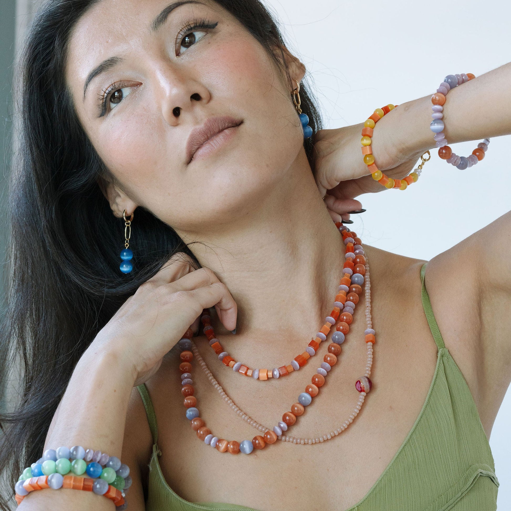 Woman wearing colorful jewelry including a necklace and bracelets against a neutral background