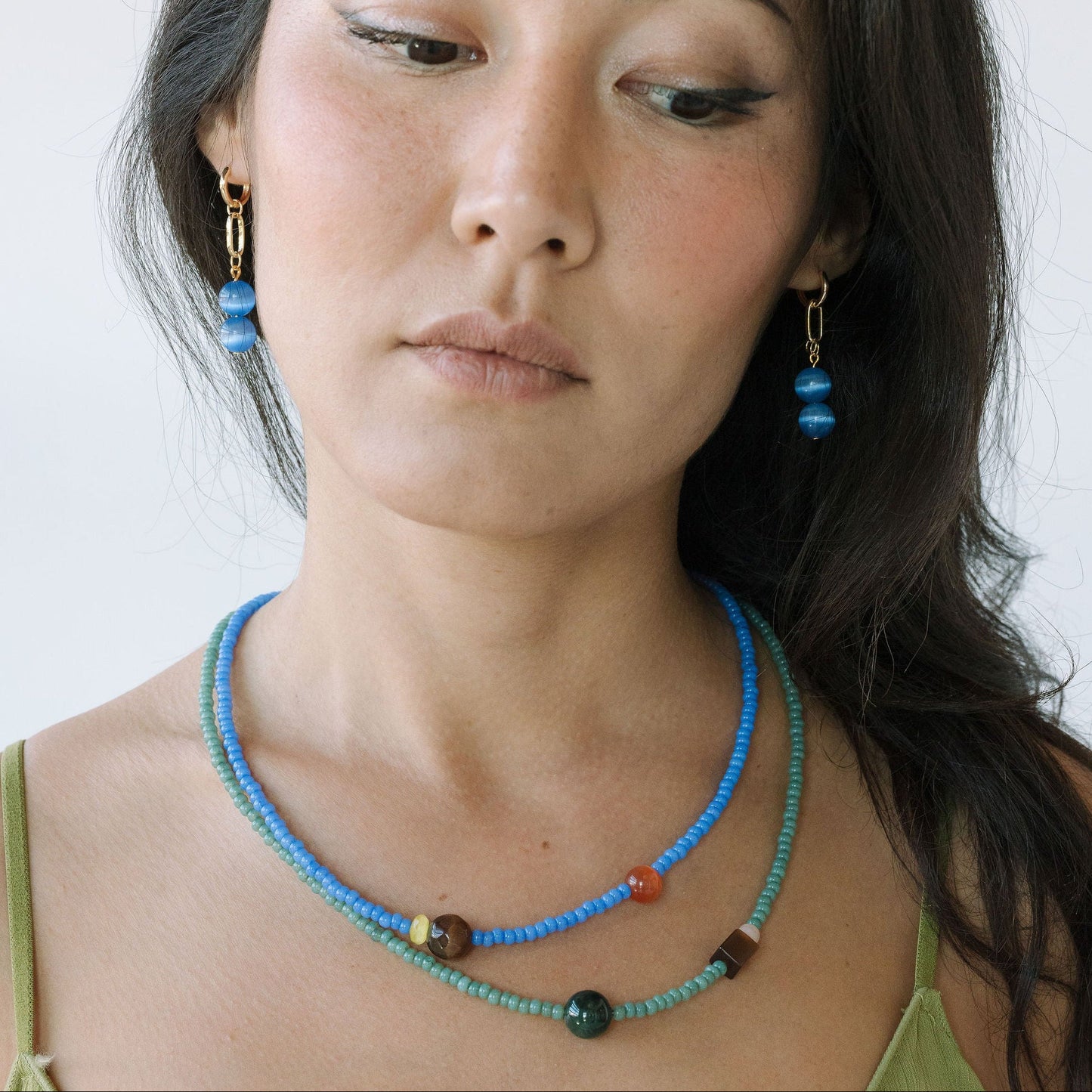 Woman wearing a blue beaded necklace and earrings against a white background