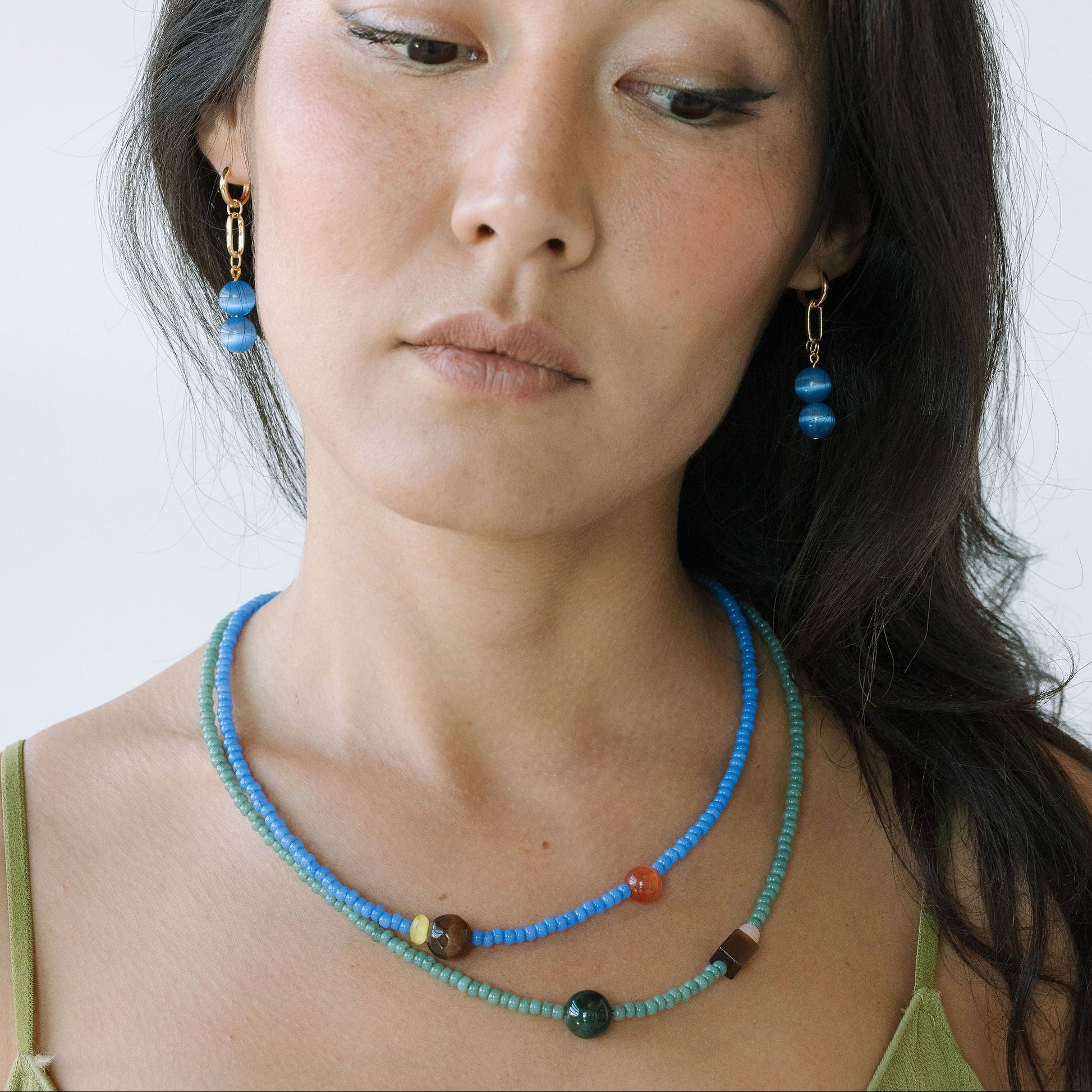 Woman wearing a blue beaded necklace and earrings against a white background