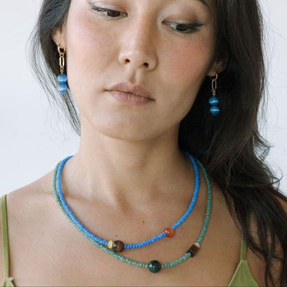 Woman wearing a blue beaded necklace and earrings against a white background