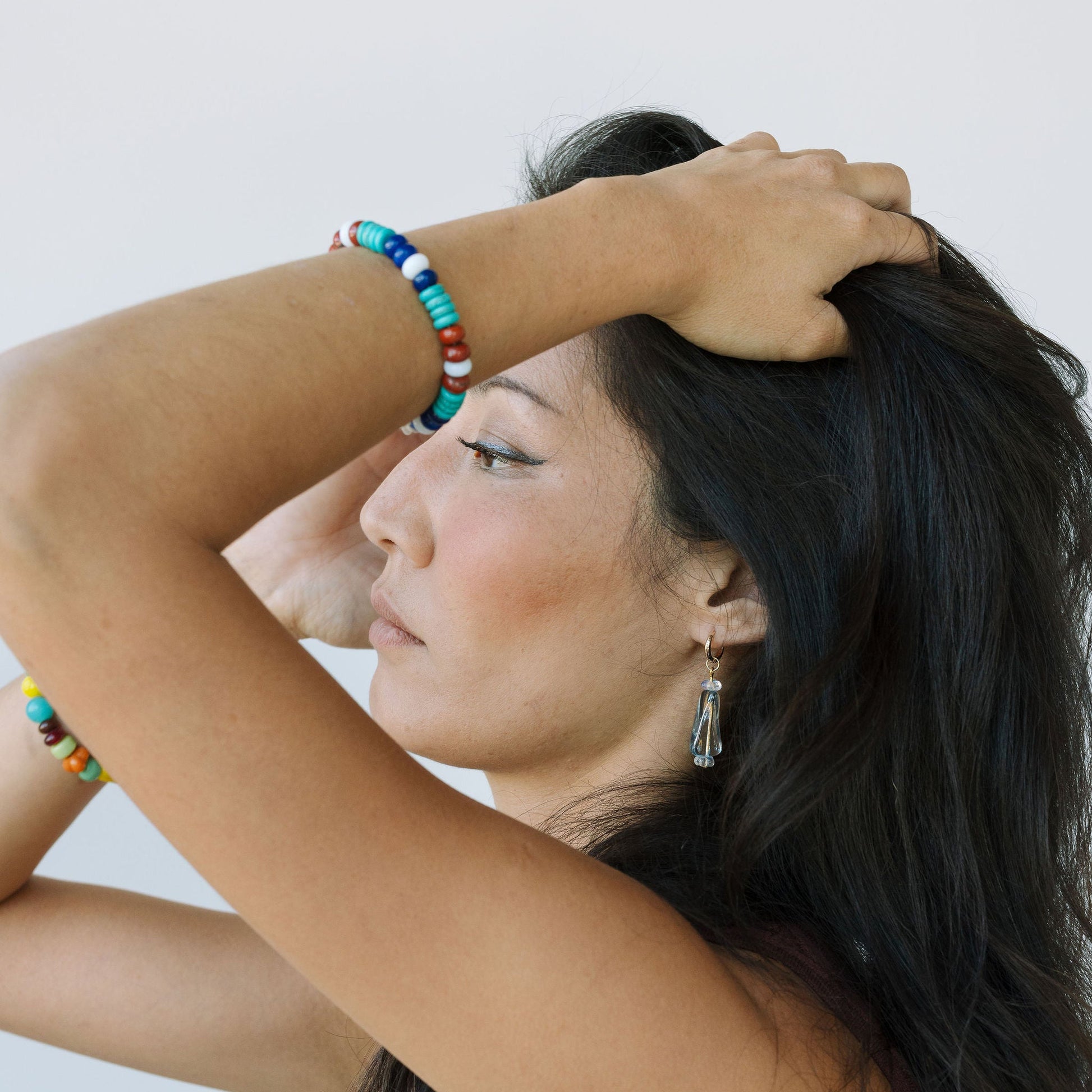 Woman with long dark hair and colorful bracelet on a plain background