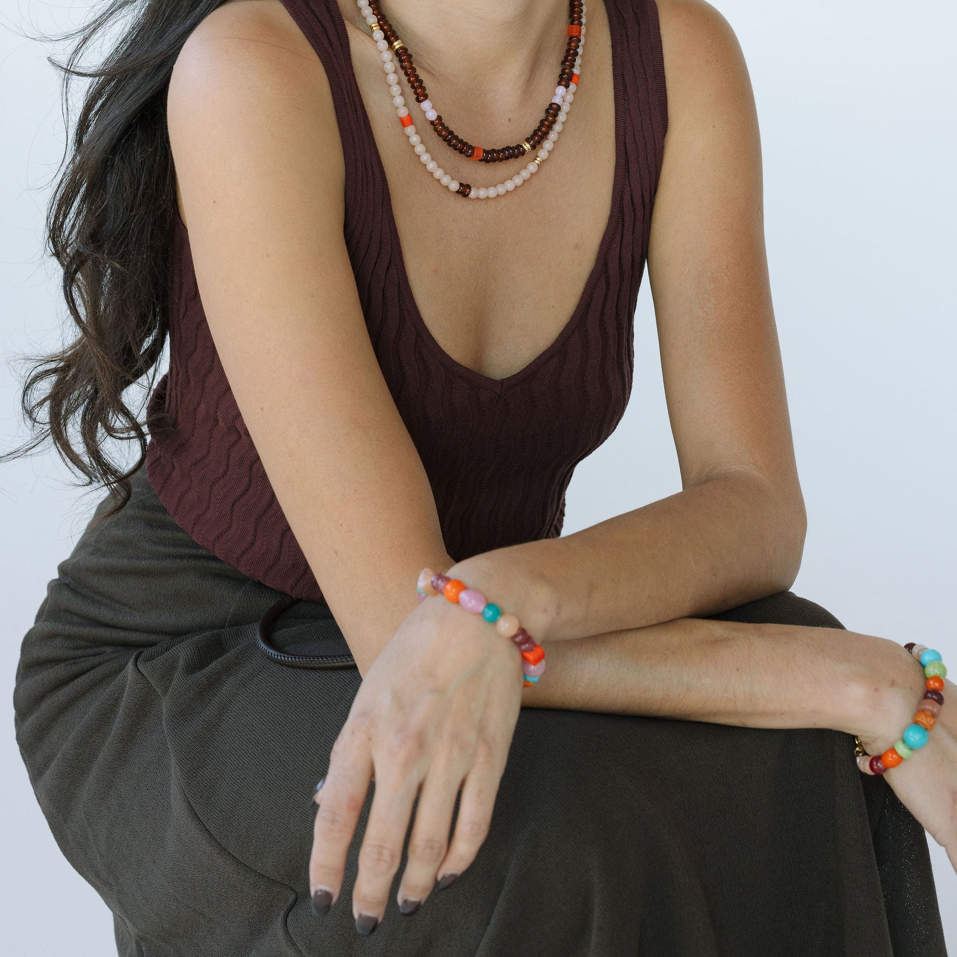 Woman wearing a brown sleeveless top and dark pants with jewelry on a white background