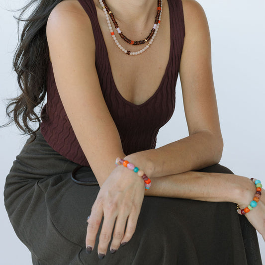 Woman wearing a brown sleeveless top and dark pants with jewelry on a white background