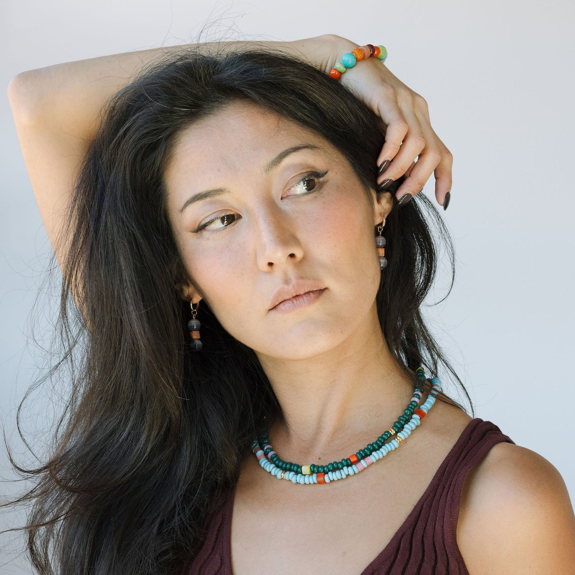 Woman with long dark hair wearing a colorful necklace against a plain background