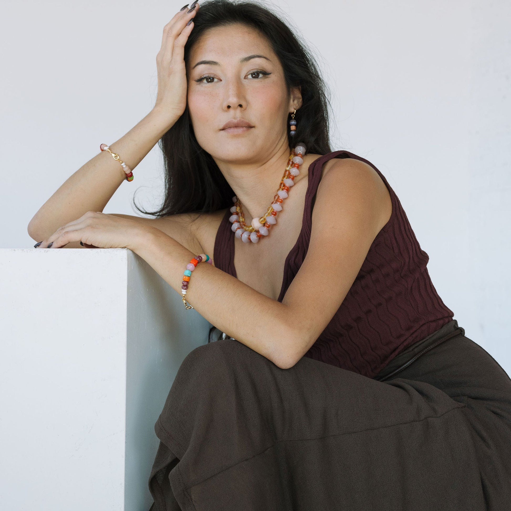 Woman sitting on a white surface wearing a brown top and dark brown pants.