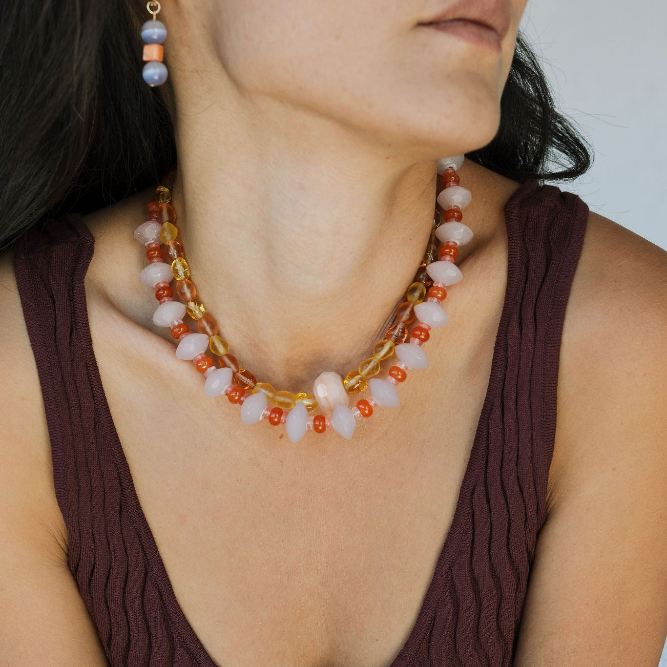 Woman wearing a gold and red beaded necklace against a neutral background