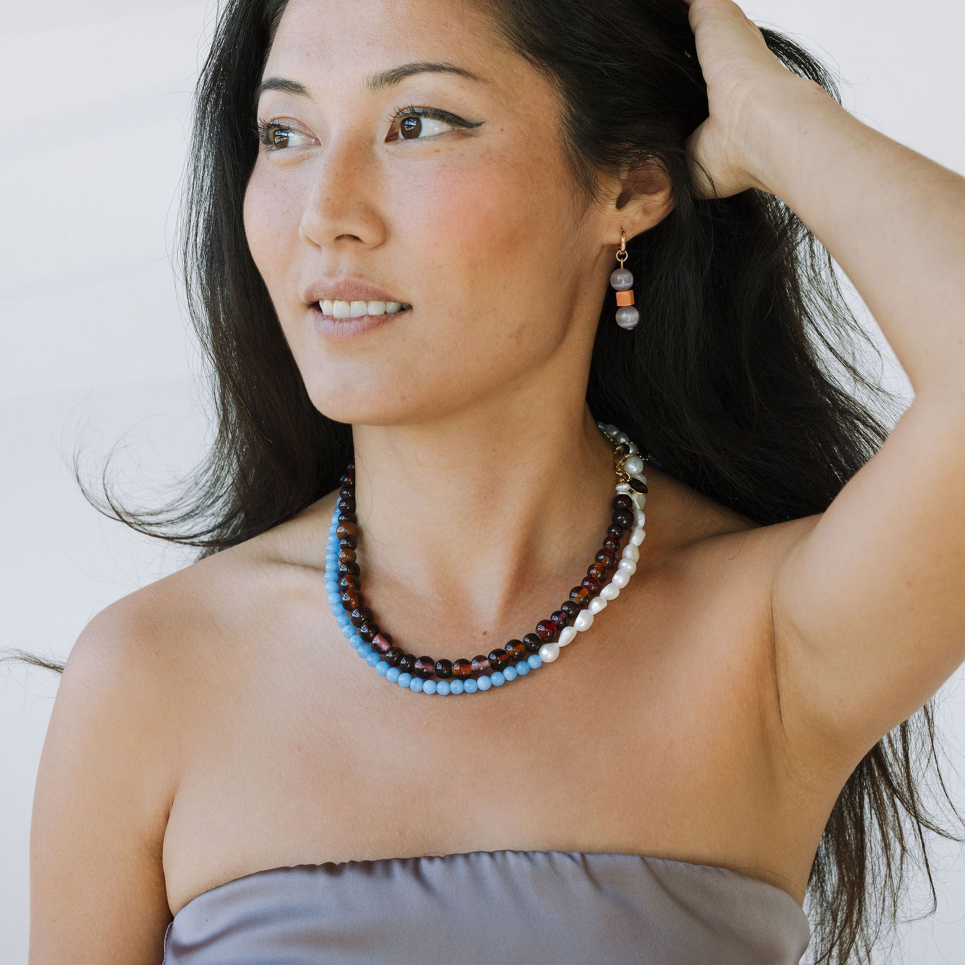 Woman wearing a beaded necklace and strapless dress against a plain background