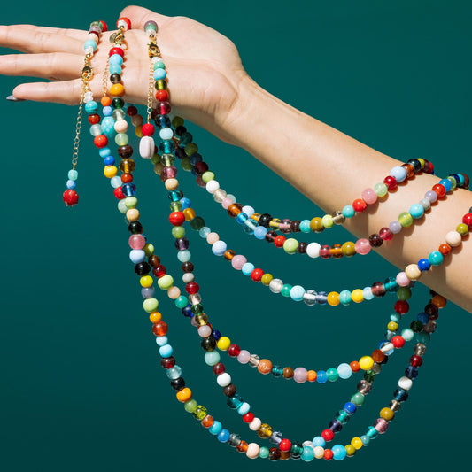 Hand holding colorful beaded necklaces against a teal background