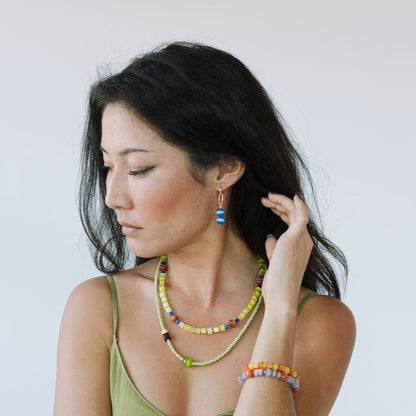 Woman wearing colorful jewelry including a necklace, earrings, and bracelets against a plain background